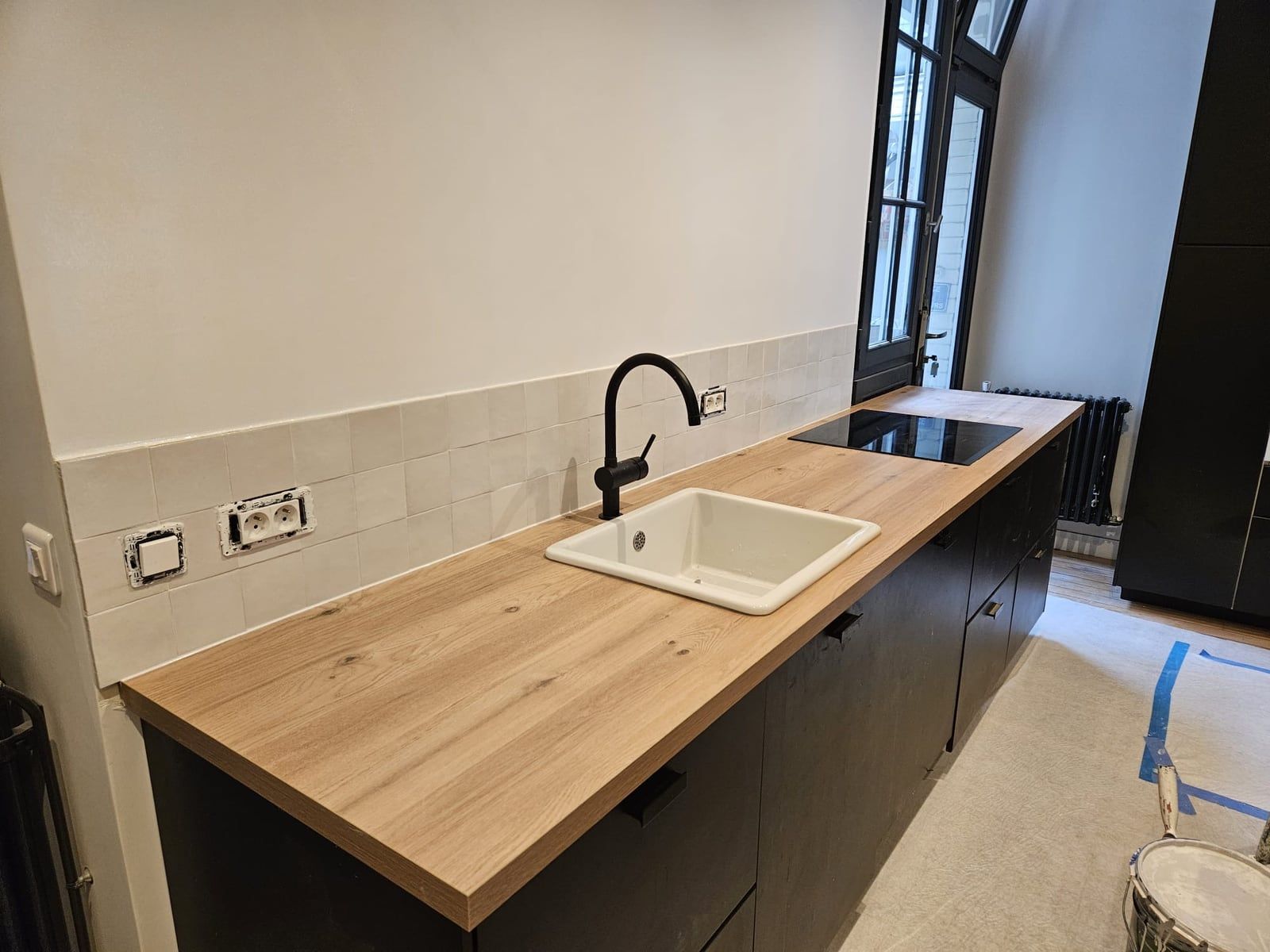 La même pièce après la pose : plan de travail en bois, meubles bas sombres et évier installé