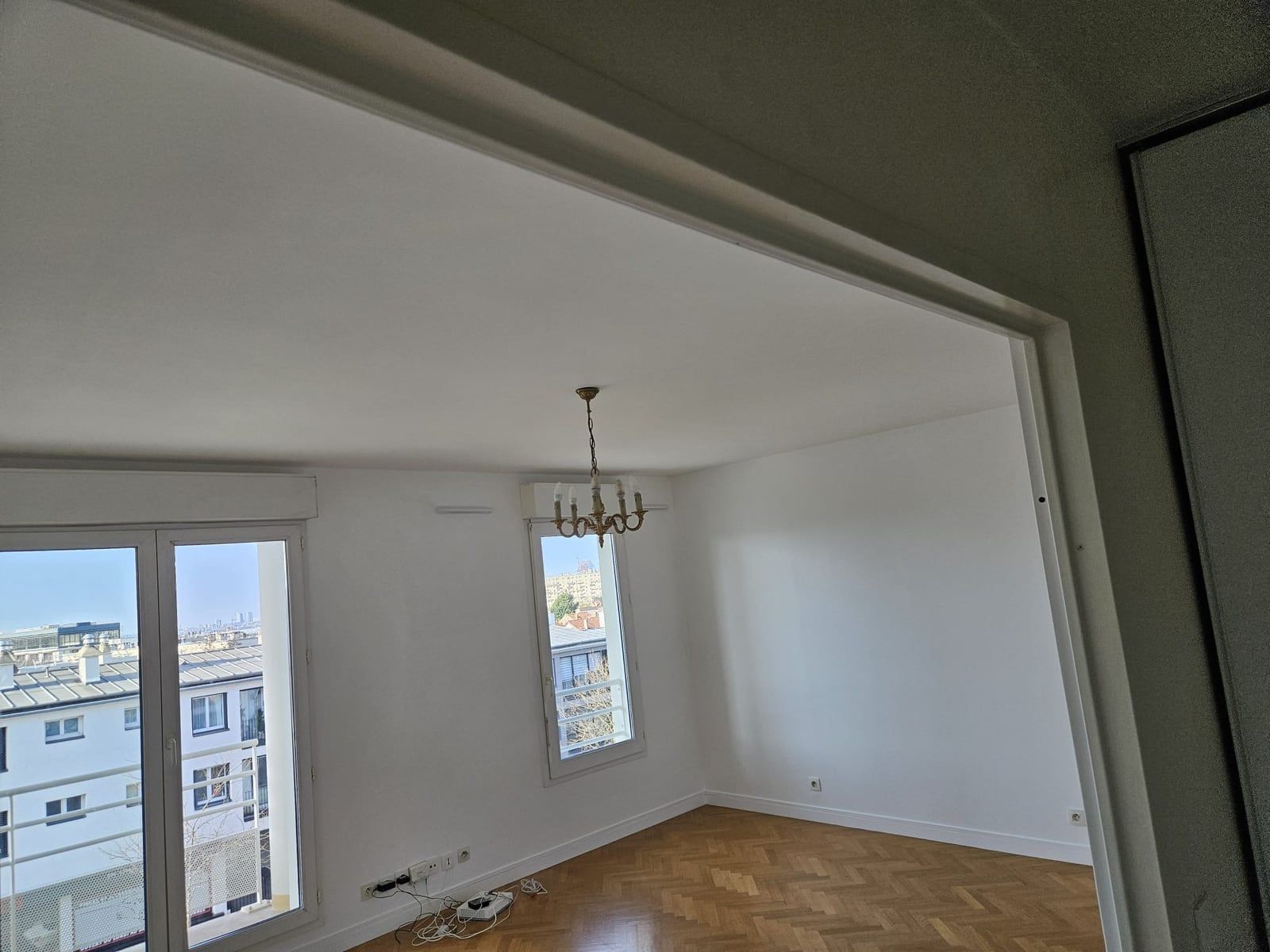 Le même séjour livré : murs et plafond blancs, parquet à bâtons rompus, lustre posé