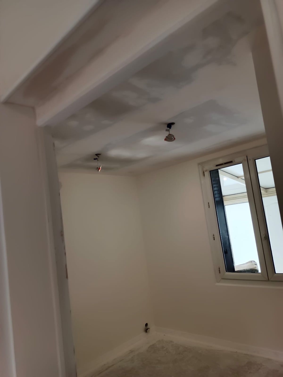 Pièce en cours de chantier : plafond en cours de reprise à l’enduit, fil électrique nu, sol brut
