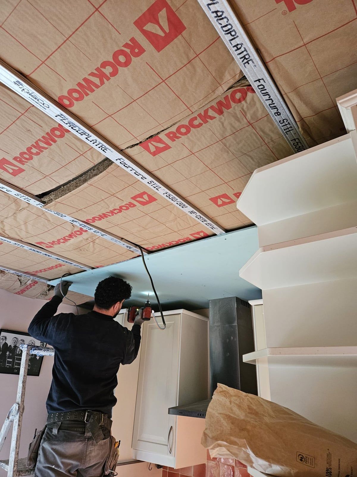 Cuisine en cours de chantier : plafond ouvert avec isolant apparent, artisan au travail
