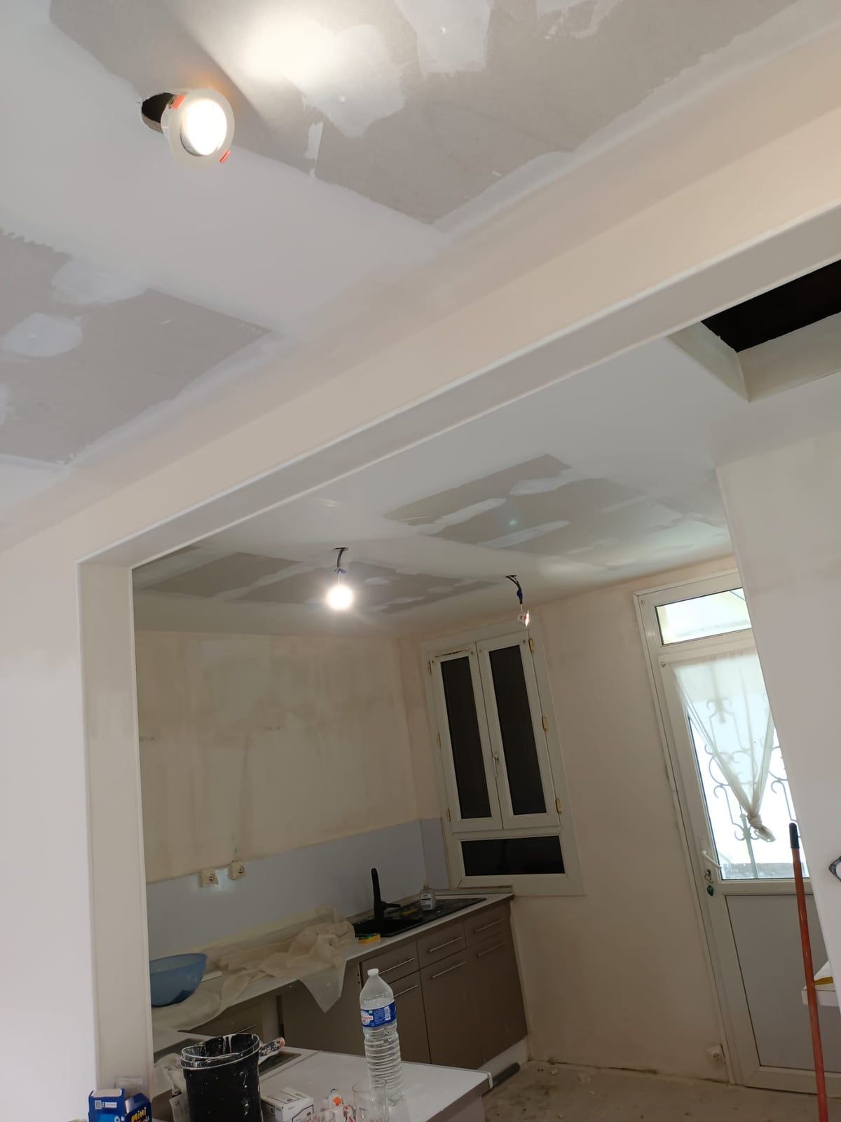 Cuisine vue depuis la pièce voisine pendant les travaux : plafond en cours d’enduit, murs bruts