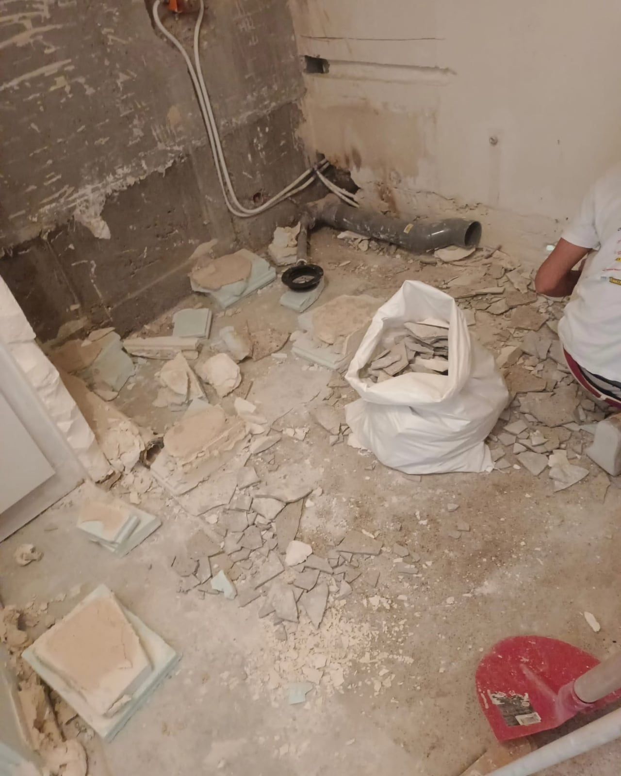 Salle d’eau entièrement démolie : sol mis à nu, gravats et anciennes canalisations apparentes