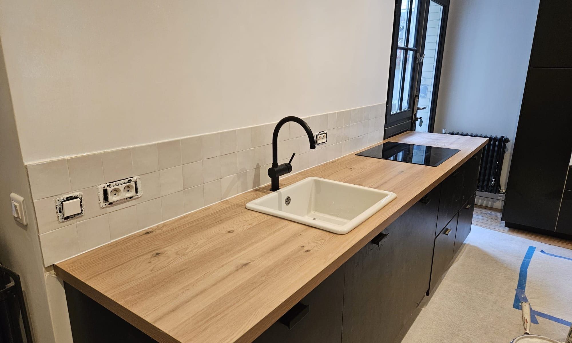 Cuisine livrée par Jarrar Rénovation : plan de travail en bois, façades noires et crédence en zellige